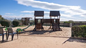 A playground with two wooden climbing structures, a slide, and two chairs. - 'Golden' Apartment with Shared Pool, Wi-Fi and Air Conditioning (Cabanas de Tavira)