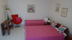 A bedroom with two beds, a chair, a small table, and a vase of flowers. - Charming and serene villa with pool, lush garden, sea and mountain view (Vamos)
