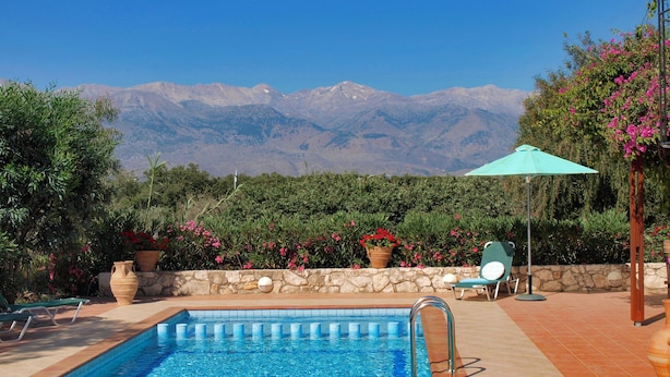 A swimming pool with a stone wall and potted plants, a lounge chair, and a view of mountains. - Charming and serene villa with pool, lush garden, sea and mountain view (Vamos)