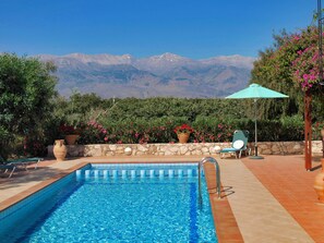 Une piscine bordée d’un mur en pierre et agrémentée de plantes en pot, une chaise longue et une vue sur les montagnes.