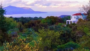 A modern white building with a red roof, surrounded by lush greenery and a mountainous backdrop. - Charming and serene villa with pool, lush garden, sea and mountain view (Vamos)