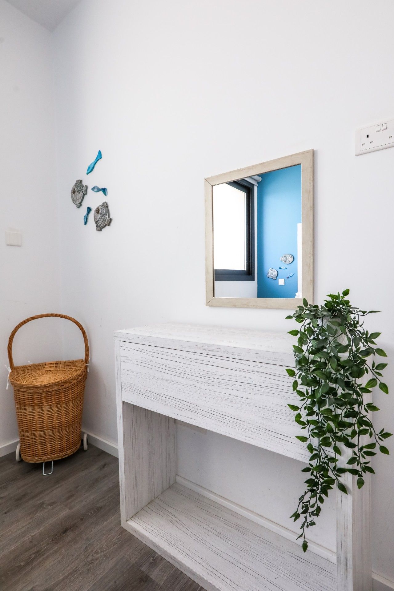 A white fireplace with a mirror above it, a wicker basket, and a green plant on the floor.