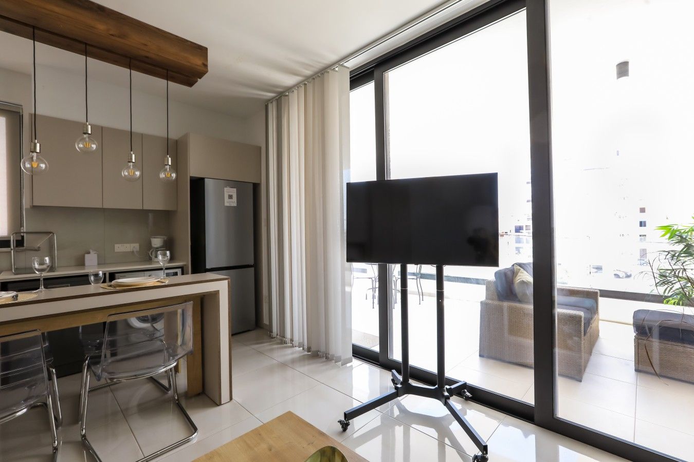 A modern kitchen with a large window, a flat-screen TV, and a dining area with chairs.