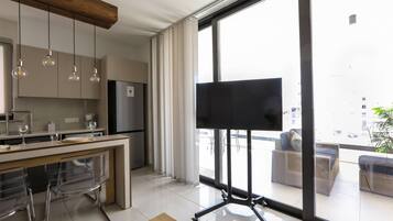 A modern kitchen with a large window, a flat-screen TV, and a dining area with chairs.