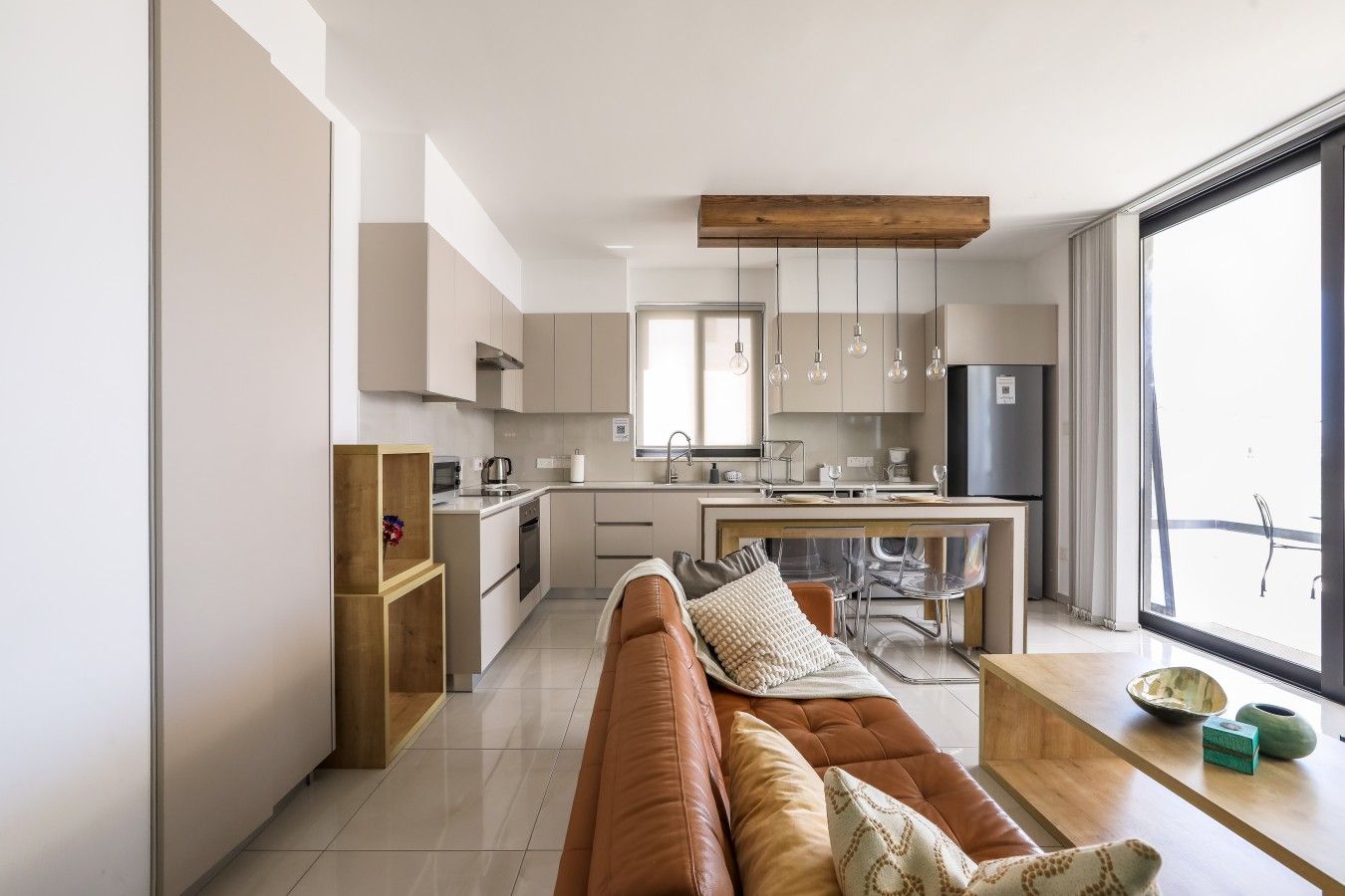 A modern kitchen with a dining area, a sofa, and a large window.