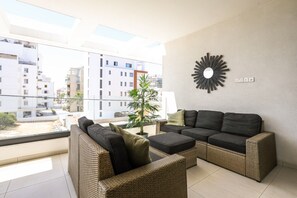 A modern living room with wicker furniture, a large window, and a view of buildings.