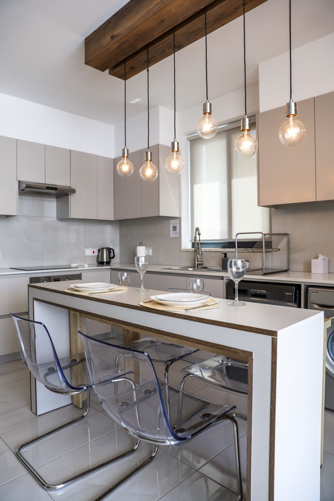Een moderne keuken met een centraal eiland, transparante glazen stoelen en hanglampen.