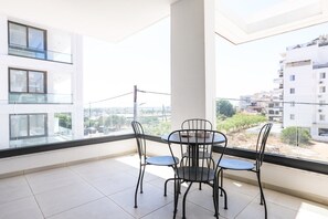 A balcony with a table and chairs, overlooking a residential area with modern buildings.