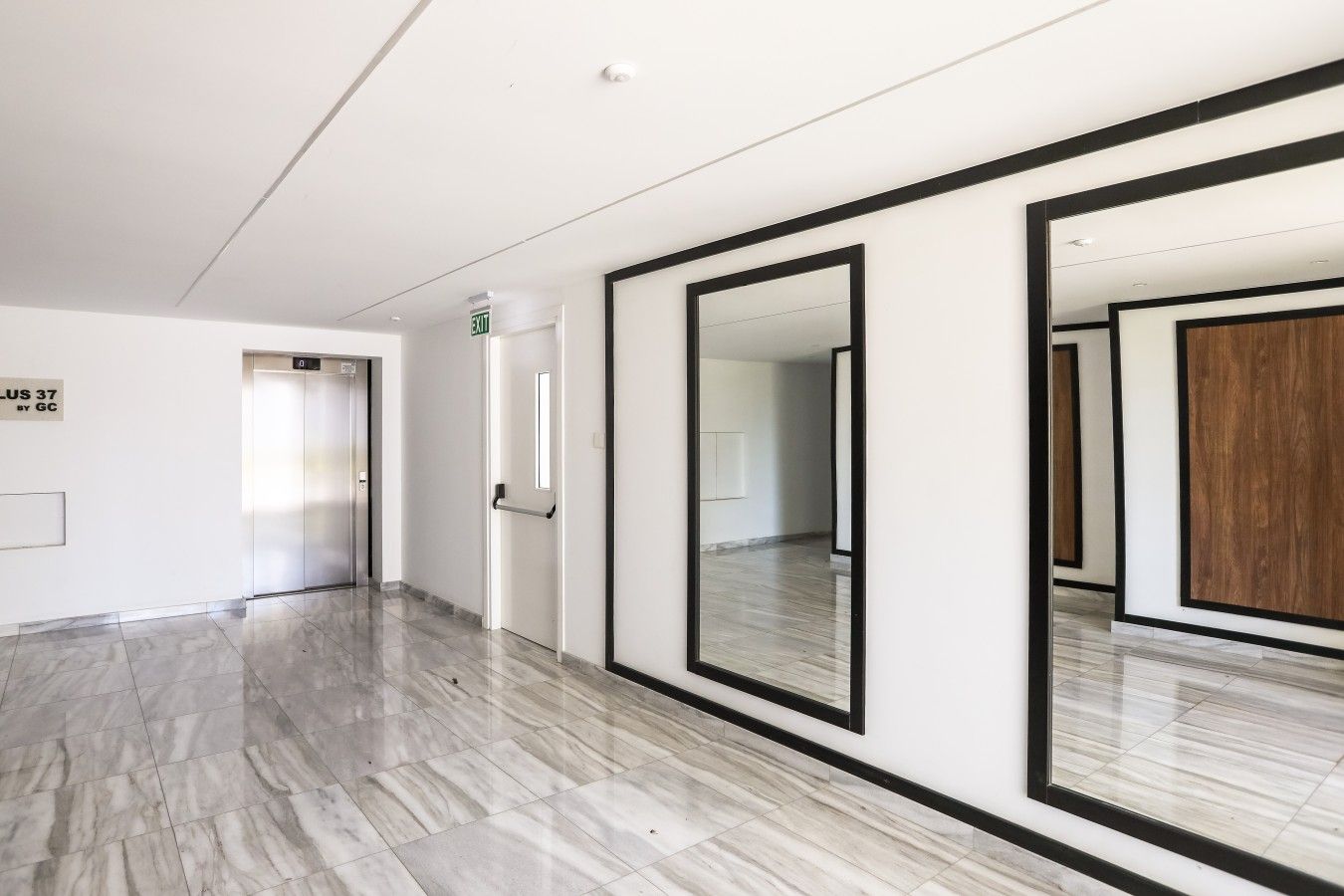 Een moderne hal met een marmeren vloer, een spiegelwand en een lift.