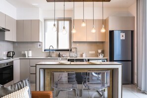 Une cuisine moderne dotée d’un îlot central, de tabourets de bar, d’un four encastré et d’un grand réfrigérateur.