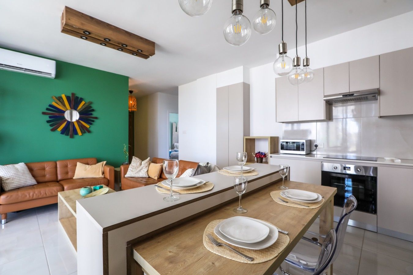 A modern kitchen with stainless steel appliances, a dining area with a wooden table and chairs, and a green accent wall.