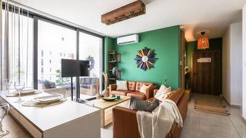 A modern living room with a large window, a flat-screen TV, a brown leather sofa, and a green accent wall.