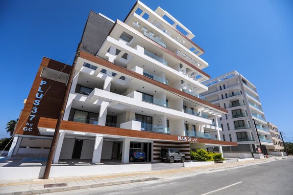 A multi-story hotel with a modern design, featuring balconies on each floor and a prominent entrance with a car parked outside.