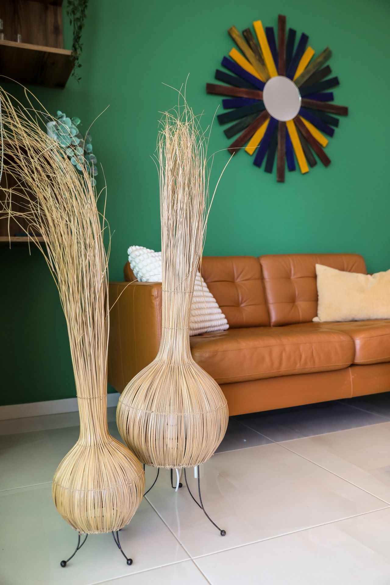 Two tall, slender vases with a natural, woven texture, placed on a tiled floor in a room with a green wall and a brown leather sofa.
