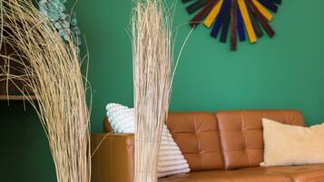 Two tall, slender vases with a natural, woven texture, placed on a tiled floor in a room with a green wall and a brown leather sofa.