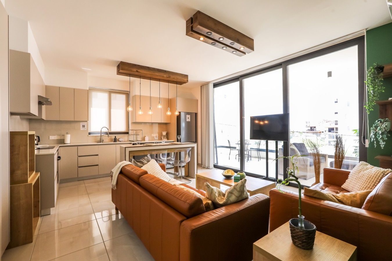 A modern kitchen with a central island, a dining area with a sofa, and a large window providing a view of the city.