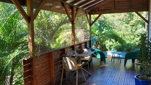 Un patio exterior con mobiliario de madera, piscina y abundante vegetación.