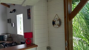 Una cocina con microondas, tostadora y una lámpara roja en la encimera. Hay una ventana con persianas y un letrero de bienvenida en la pared.