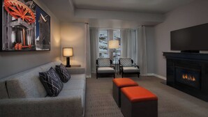 Un salon moderne avec un canapé gris, des coussins à motifs, une cheminée, un téléviseur à écran plat et un grand tableau accroché au mur.