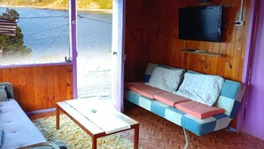 Une pièce avec un plancher en bois, un canapé avec des coussins, une petite table et un téléviseur fixé au mur.