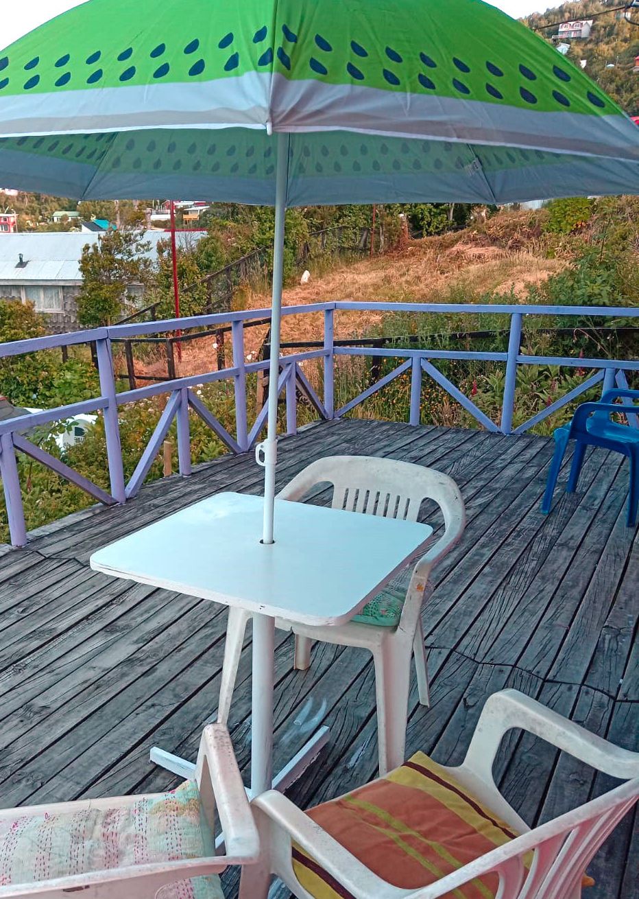 Une terrasse en bois avec une table et des chaises, une rambarde violette et un parasol vert.