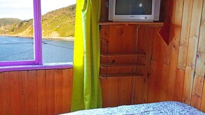 Une cabine comprenant un lit, un téléviseur posé sur une étagère et une fenêtre avec des rideaux.