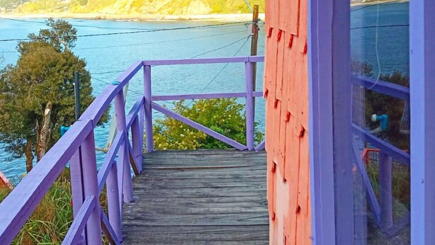 Une terrasse en bois avec des rampes violettes qui mène à un bâtiment rouge doté de grandes fenêtres.