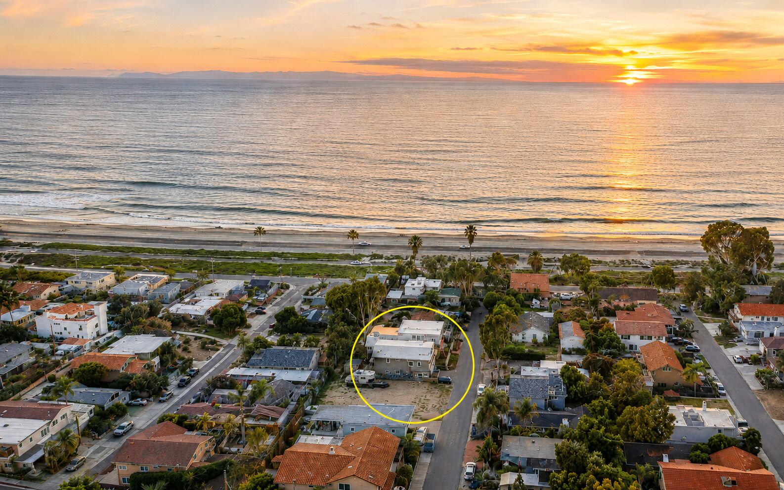 An aerial view of a coastal residential area with houses, roads, and palm trees.