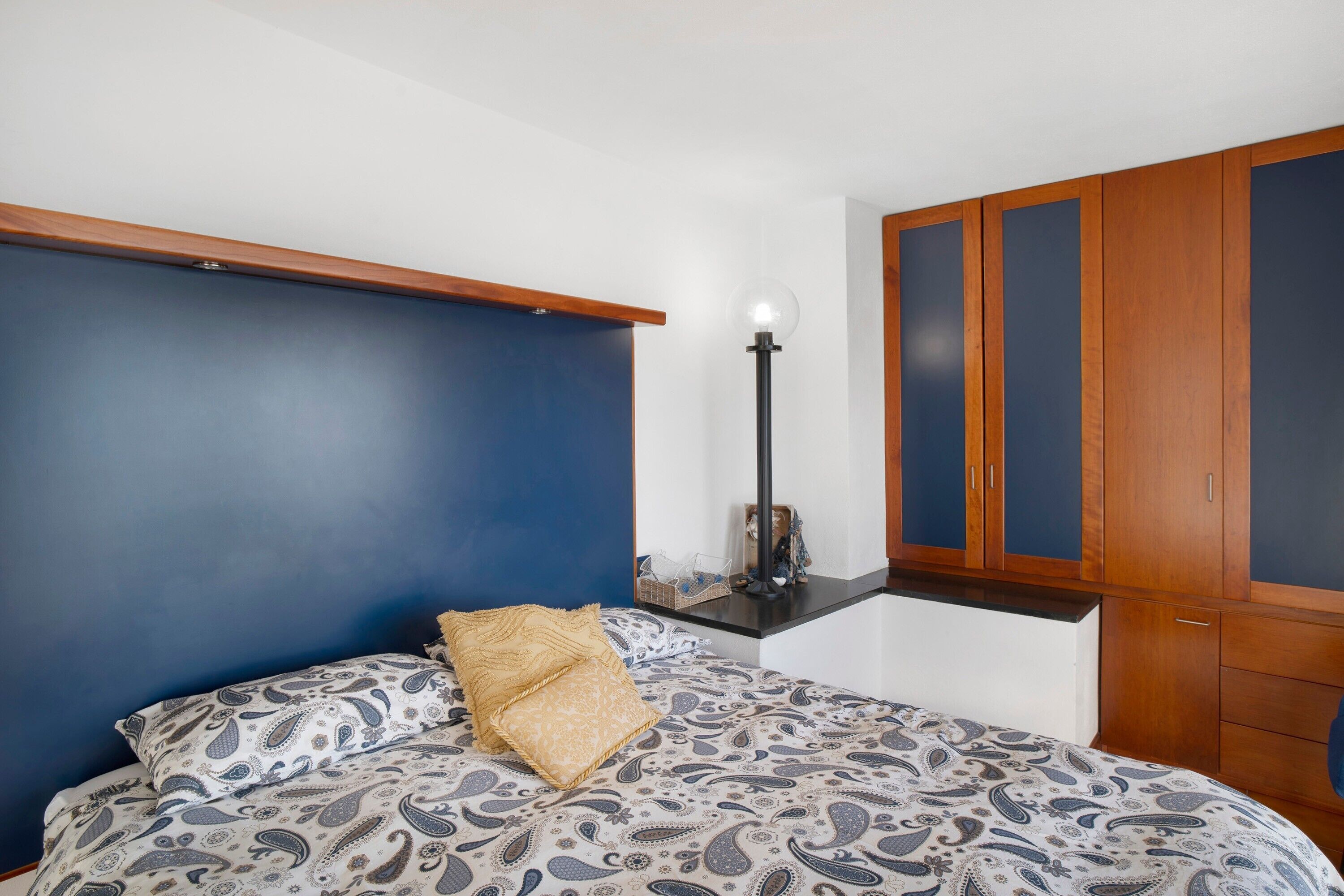 Quarto com cama, mesa de cabeceira, abajur e guarda-roupa.