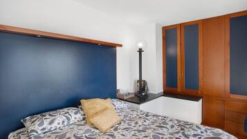 Quarto com cama, mesa de cabeceira, abajur e guarda-roupa.