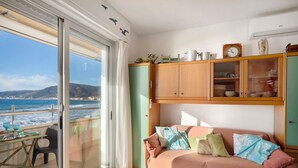 Een balkon met uitzicht op zee, een bank met kussens en een houten kast met glazen deuren.
