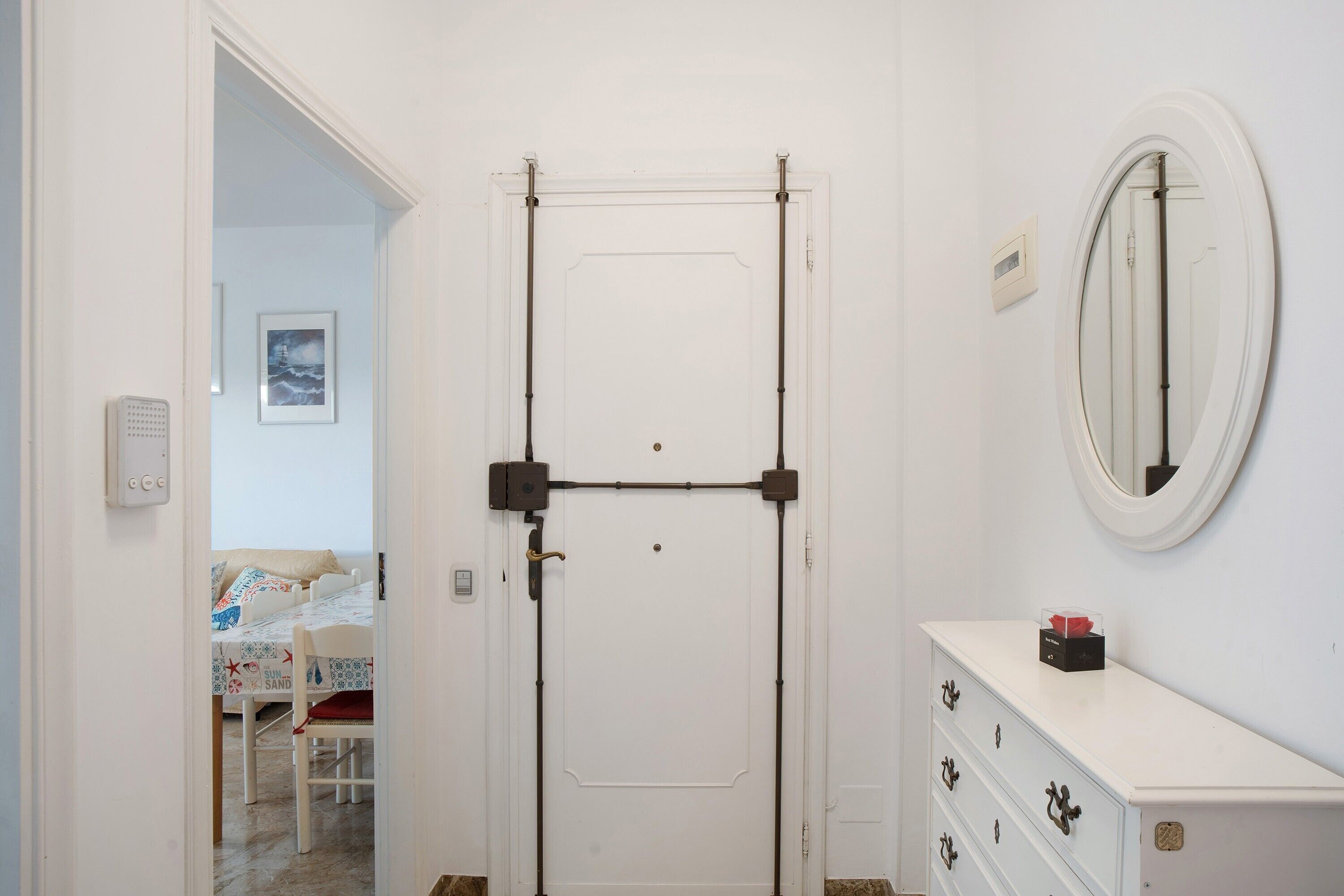 A room with a white door, a dresser with drawers, a mirror, and a bed with a patterned bedspread.