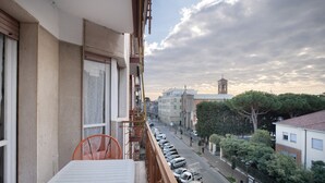 A balcony with a white table and orange chair, overlooking a street with parked cars and buildings.