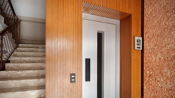 A wooden staircase with a metal railing, a white door with a black handle, and a textured wall.