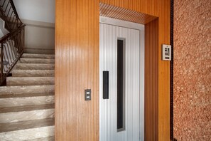 A wooden staircase with a metal railing, a white door with a black handle, and a textured wall.