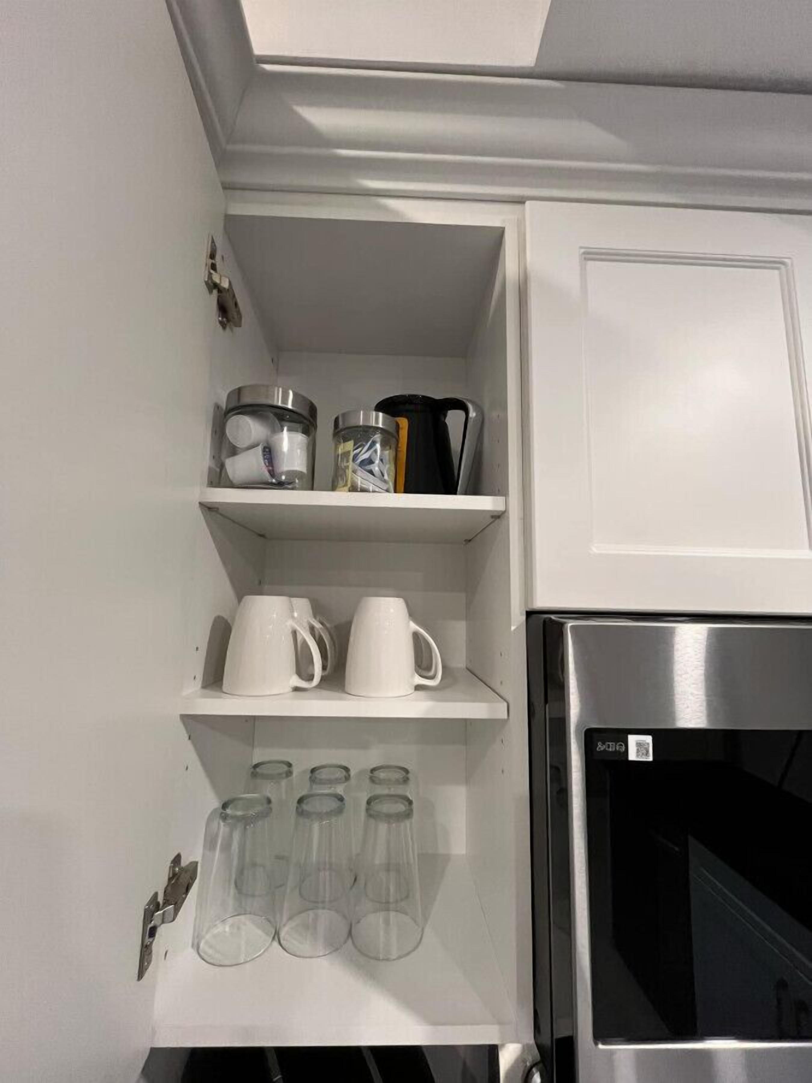 A kitchen with white cabinets, a stainless steel refrigerator, and shelves holding kitchenware.