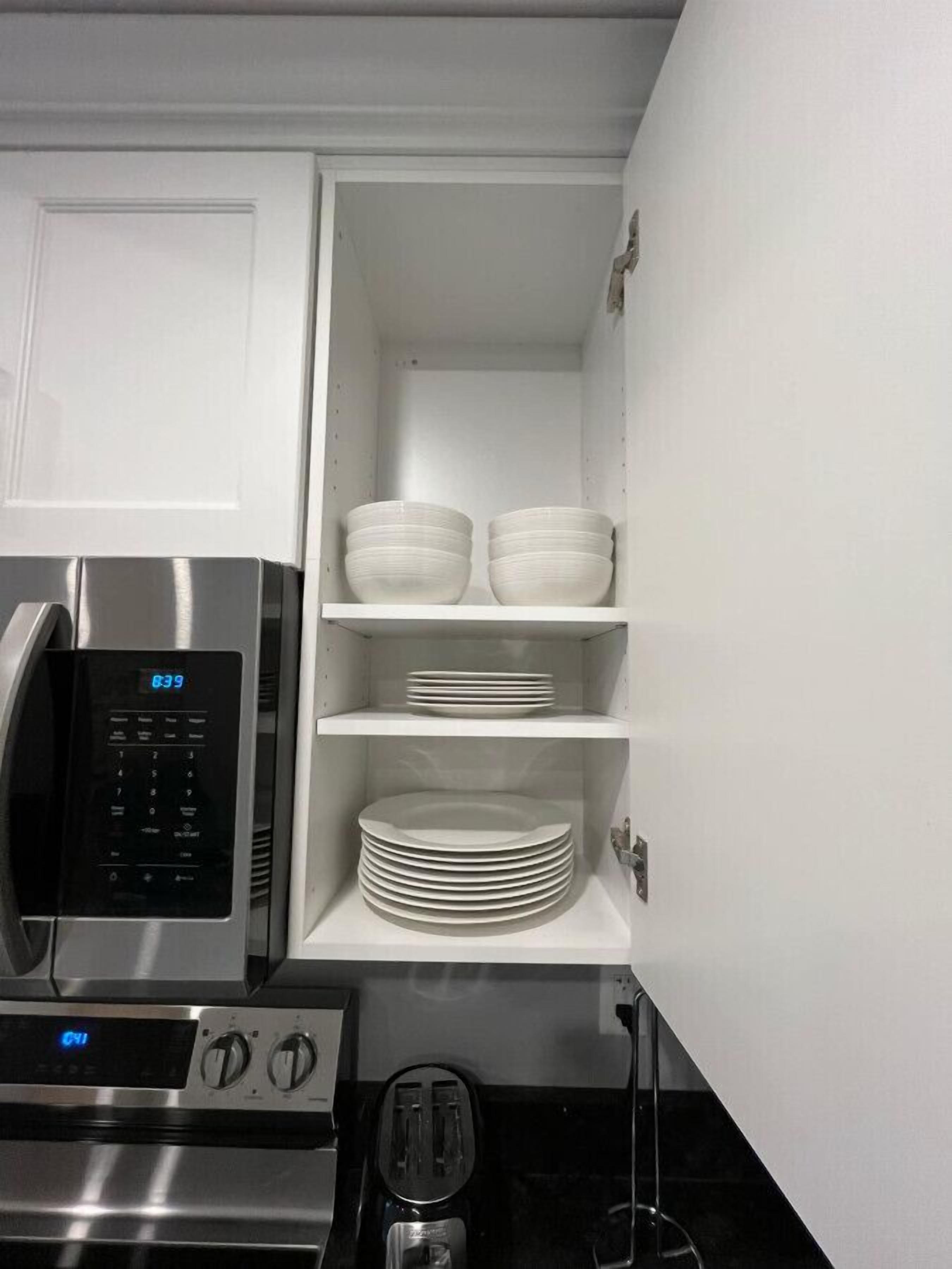 A kitchen with a microwave, toaster, and shelves with white bowls and plates.