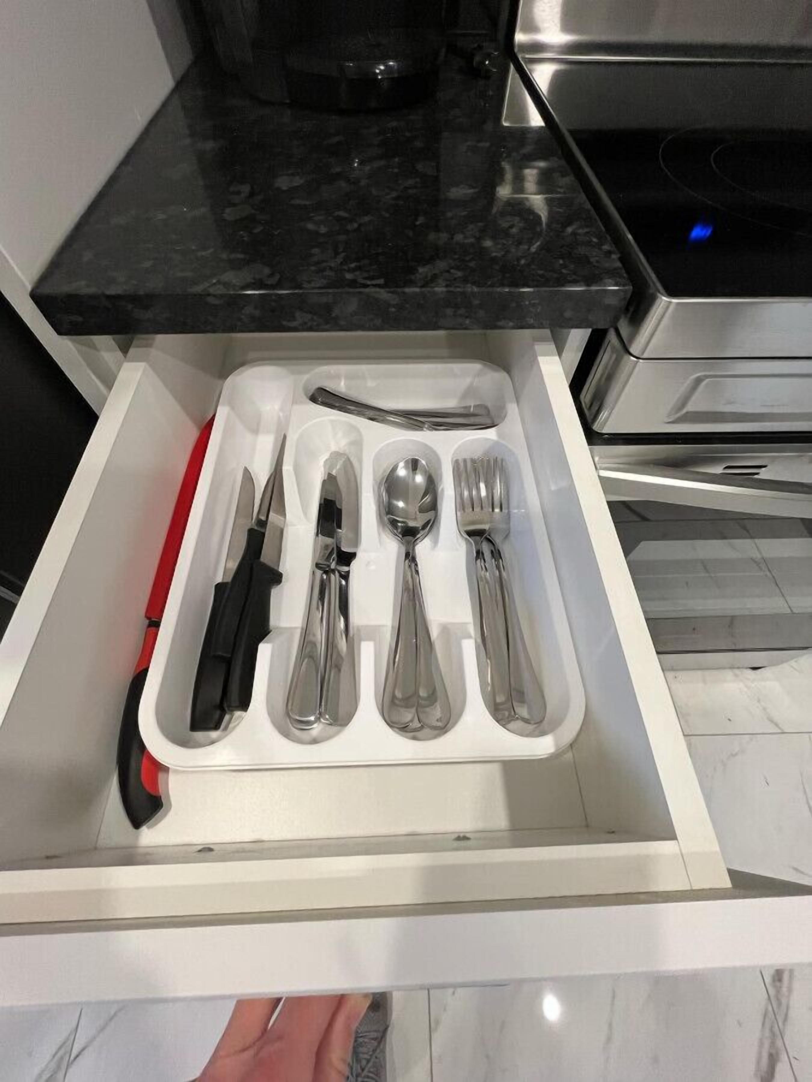 Un tiroir contenant un couteau, une cuillère, une fourchette et un ustensile à manche rouge.