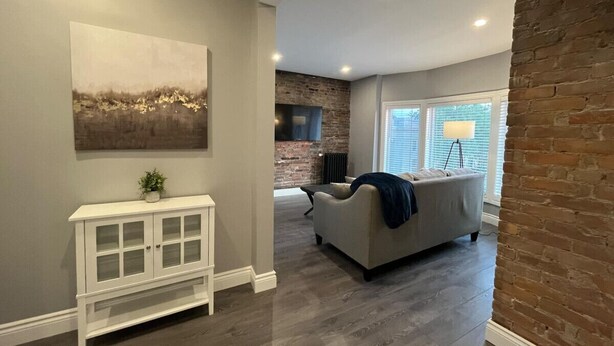 Ein Wohnzimmer mit grauem Sofa, weißem Konsolentisch und einer Wand mit Backsteinverkleidung.