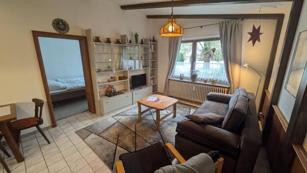 Un soggiorno accogliente con un divano, un tavolino e una televisione. Si nota una libreria, una finestra con tende e una decorazione a stella sul muro.