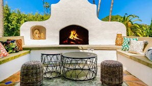 An outdoor patio with a stone fireplace, two round metal tables, wicker ottomans, and a cushioned seating area with patterned cushions. - Last Minute Deals/A/C/Hot Tub/Great Family Home (La Jolla)