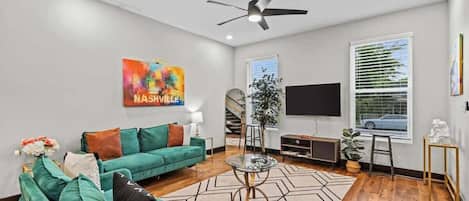 A modern living room with a teal sofa, a glass coffee table, and a ceiling fan.