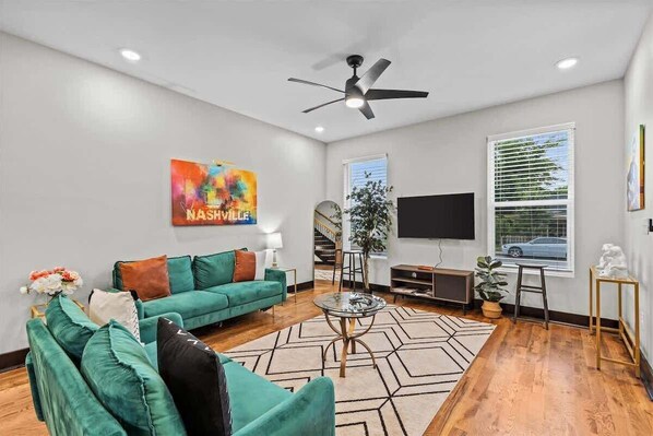 A modern living room with a teal sofa, a glass coffee table, and a ceiling fan.