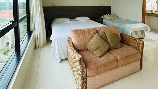 Una habitación de hotel con un ventanal grande, una cama, un sofá y una mesita.