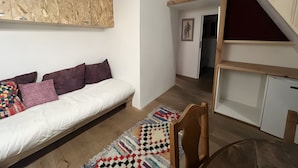 A room with a bed, a wooden headboard, a wall-mounted shelf, a door leading to another room, and a small table with a chair. - Apartment 'Au Soleil' with Mountain View, Private Garden and Wi-Fi (seez)