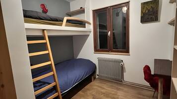 Une petite pièce comprenant un lit superposé, une échelle, un bureau, un radiateur et une fenêtre.