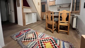 A compact kitchen with wooden cabinets, a dining table with chairs, a small refrigerator, and a staircase. - Apartment 'Au Soleil' with Mountain View, Private Garden and Wi-Fi (seez)
