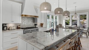 Een ruime keuken met witte kastjes, een groot kookeiland en hangende pendantlampen.