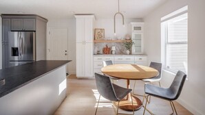 Una cuina moderna amb una illa central, armaris blancs i una zona de menjador amb una taula rodona i cadires.