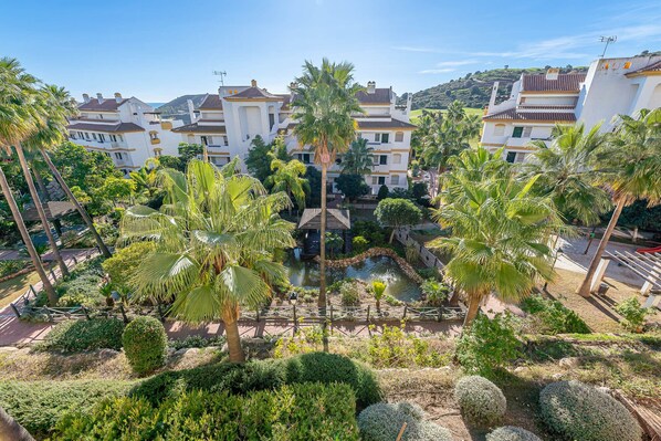 Surrounded by lush greenery and palm trees, this tranquil oasis features a central water feature and traditional Mediterranean-style buildings.